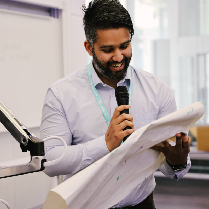 Shahid, an In2research participant, speaking into a microphone while reading notes for a group presentation.